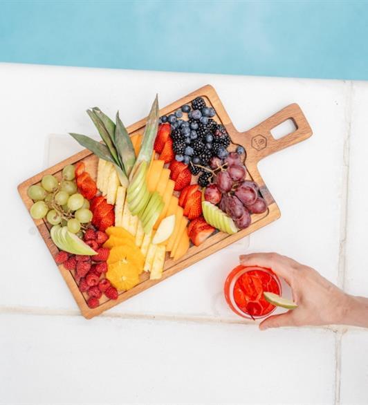 A plate of fruit and a fruity drink by the pool
