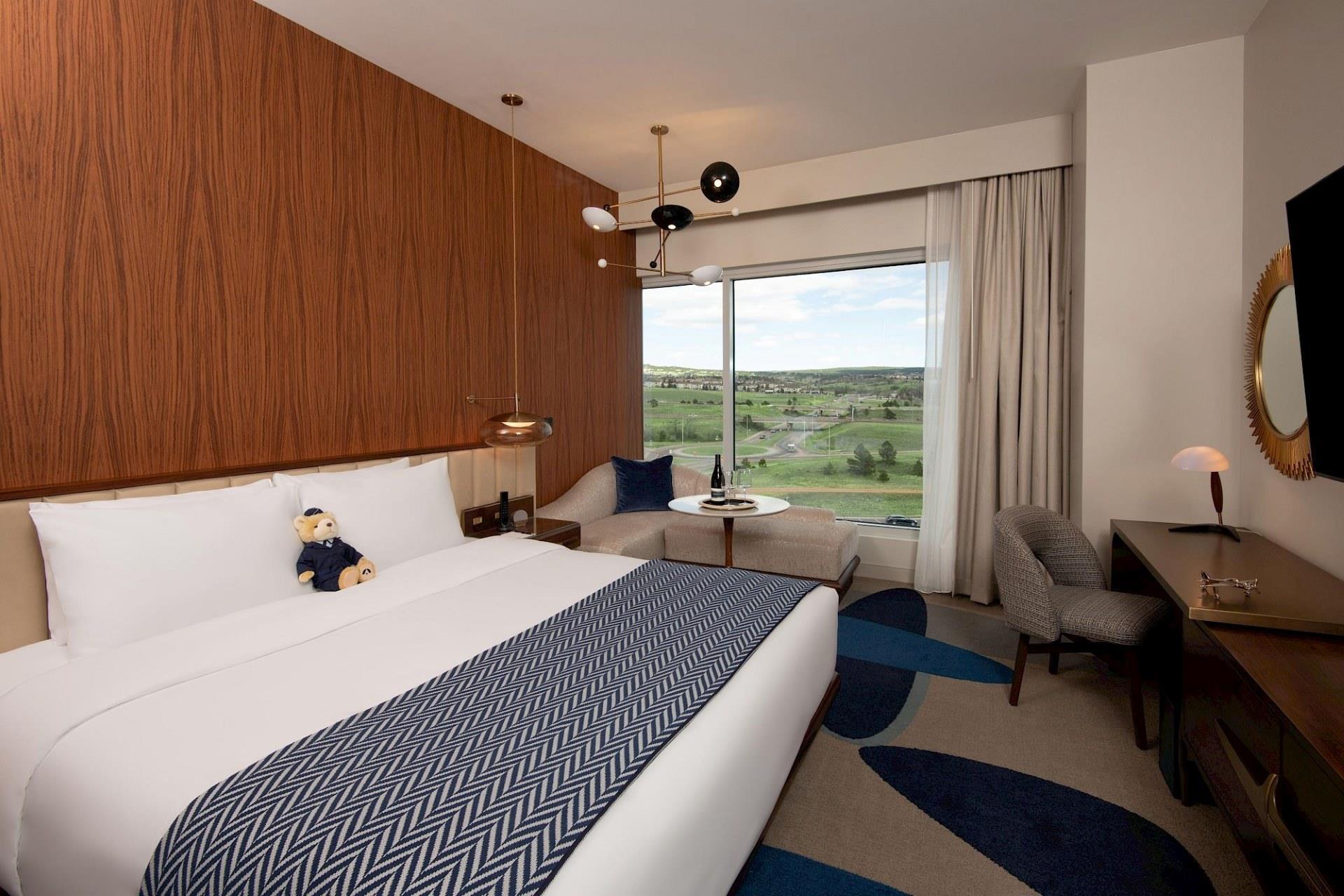 Club-level king room with white bedding, blue headboard, patterned throw, wood slat paneling, blue desk chair, framed artwork, and floor-to-ceiling window.
