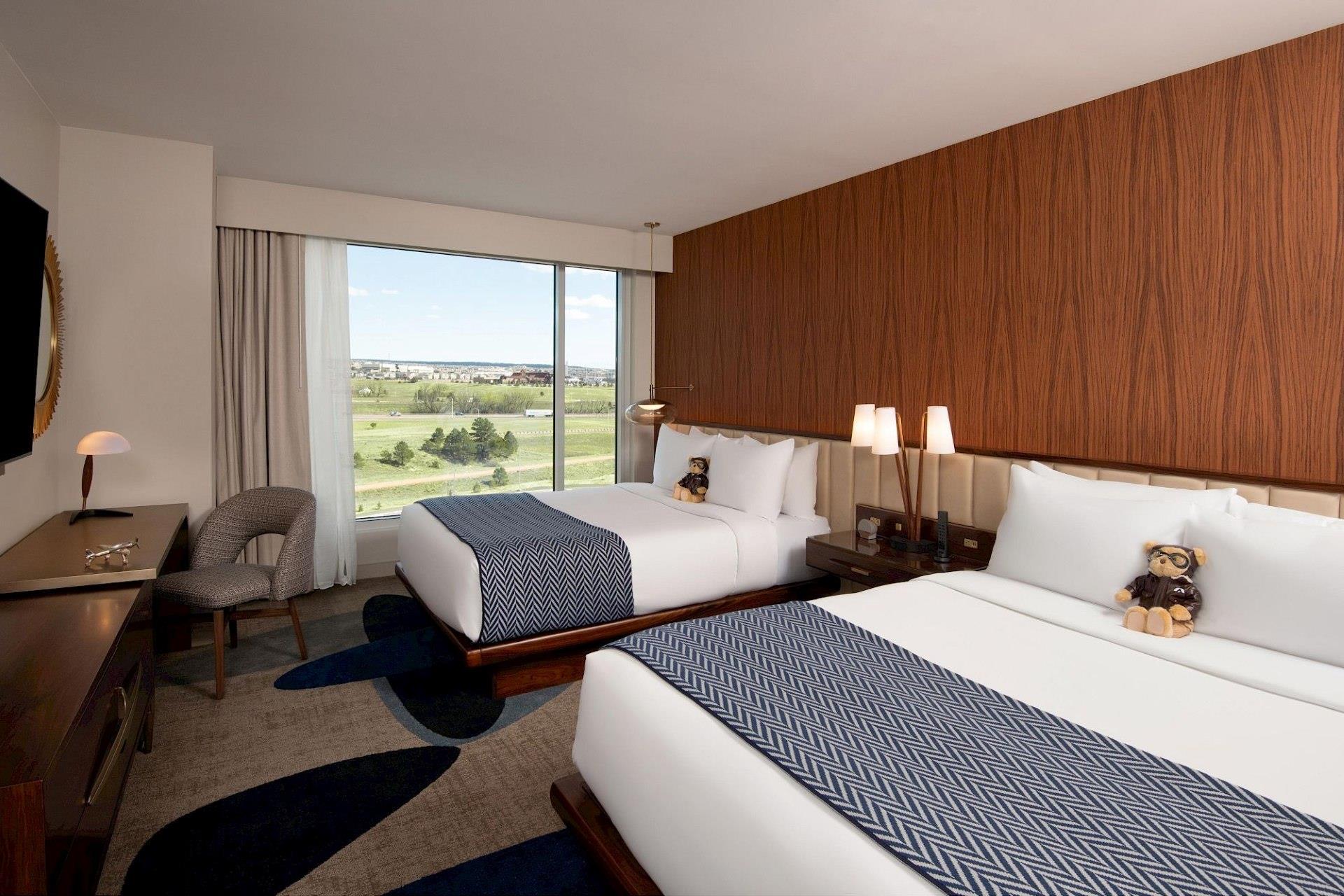 Club-level room with two white beds, blue patterned throws, warm wood accent wall, large window, desk, and neutral upholstered chair.
