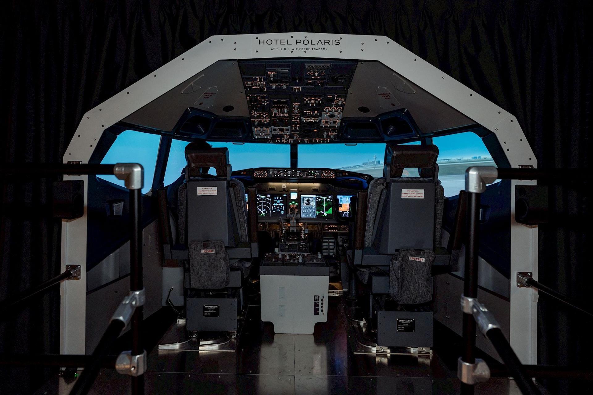 Commercial flight simulator at Hotel Polaris featuring a full-scale aircraft cockpit with dual pilot seats, illuminated flight controls, and an immersive runway simulation experience.