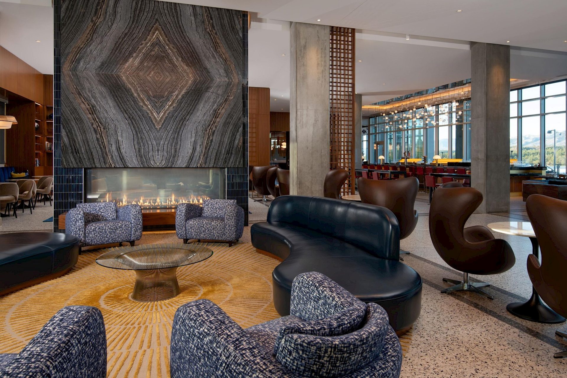 Hotel Polaris lobby lounge featuring a dramatic stone fireplace, contemporary seating, and an open-concept design connecting to the hotel's restaurant and bar with views of the Colorado landscape.
