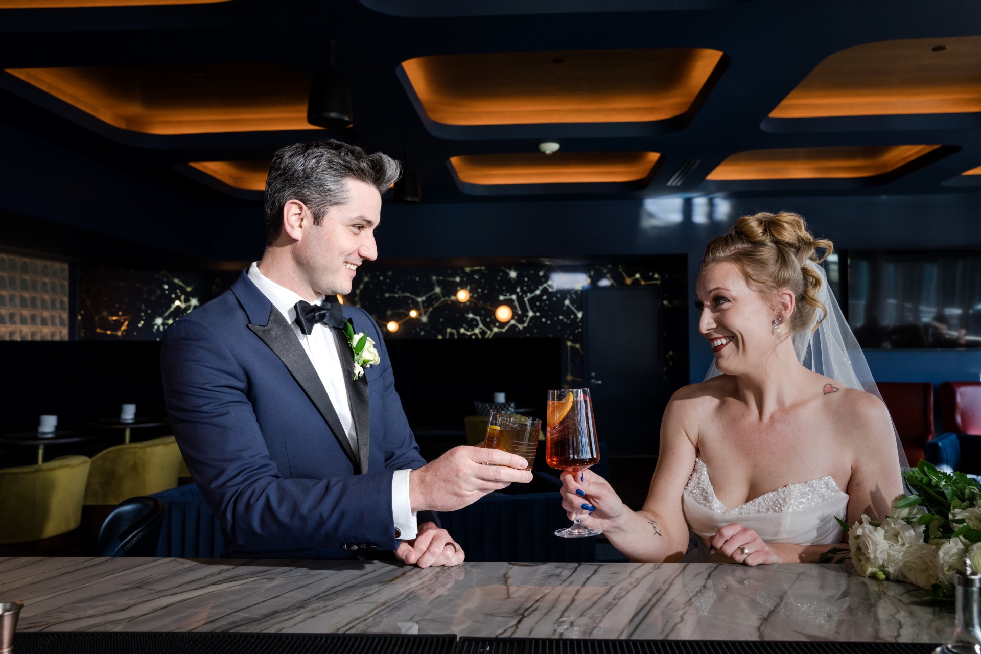 Bride and groom toasting cocktails at The Aviator rooftop bar at Hotel Polaris, celebrating their wedding in an elegant aviation-inspired setting.