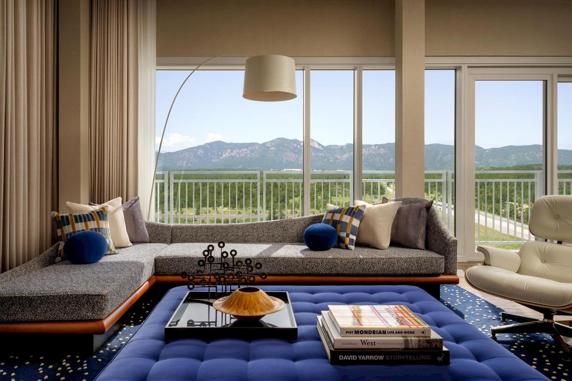 Luxury suite at Hotel Polaris featuring a contemporary lounge with designer furnishings, floor-to-ceiling windows, a private balcony, and panoramic views of the Rocky Mountains.