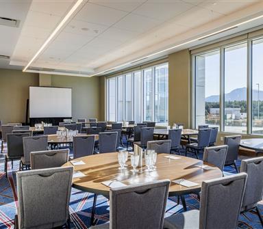 Meeting room at Hotel Polaris set for a conference with round tables, presentation screen, floor-to-ceiling windows, and scenic views of the Rocky Mountains.