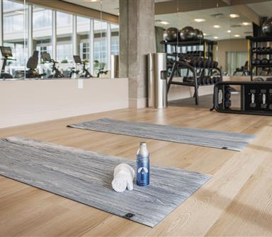 Fitness center at Hotel Polaris featuring a dedicated stretching area with yoga mats, free weights, cardio equipment, and floor-to-ceiling mirrors in a bright, modern workout space.