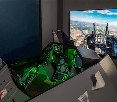 Fighter jet flight simulator at Hotel Polaris featuring a realistic cockpit with illuminated controls and a large display showing an immersive aerial flight experience.
