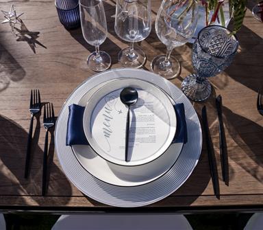 Elegant wedding place setting at Hotel Polaris featuring white dinnerware, navy napkin, black flatware, crystal glassware, and a printed menu on a wooden table.