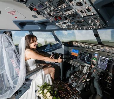 Bride seated in the cockpit of Hotel Polaris' commercial flight simulator, smiling as she operates the controls while wearing a wedding dress and veil.