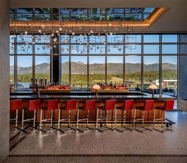 Hotel Polaris lobby bar featuring modern red bar stools, contemporary lighting, floor-to-ceiling windows, and panoramic views of the Rocky Mountains.