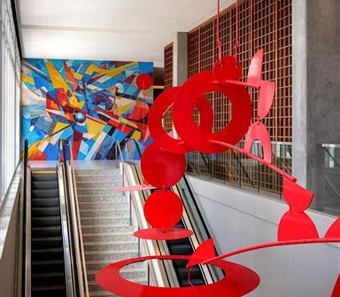 Red suspended sculpture above escalators at Hotel Polaris, with a colorful aviation-inspired mosaic in the background.