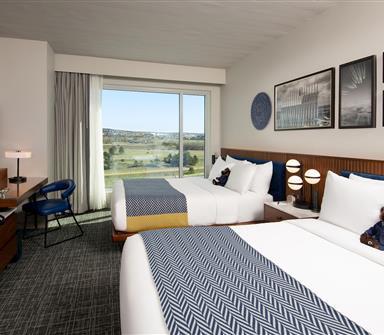 Double queen guest room at Hotel Polaris featuring modern aviation-inspired décor, plush bedding, a workspace, in-room coffee station, and large windows with views of the surrounding Colorado landscape.